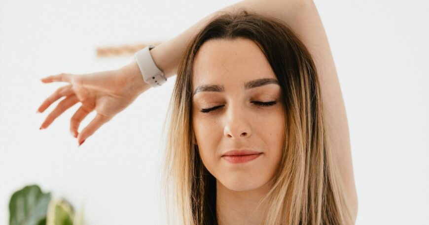 Kvinde med lukkede øjne trækker dybt vejret gennem næsen, arm løftet i afslappet mindfulness