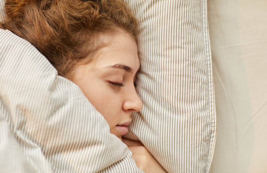 Ung kvinde sover i stribet dyne med hoved på pude, rolig sideprofil