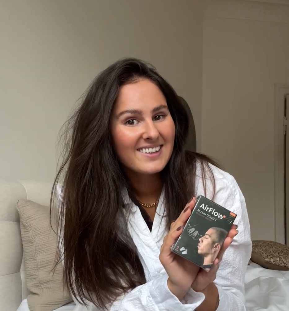 Smilende kvinde holder AirFlow+ nasal dilatoræske, nærbillede af produkt i hjemmemiljø