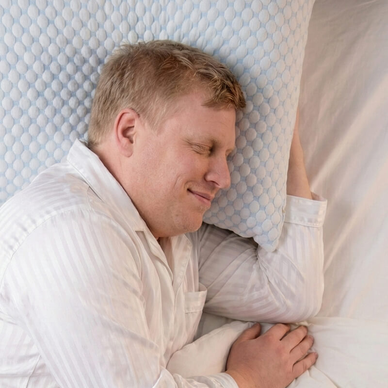 Mand i hvide pyjamas sover afslappet på en lyseblå mønstret pude med let smil