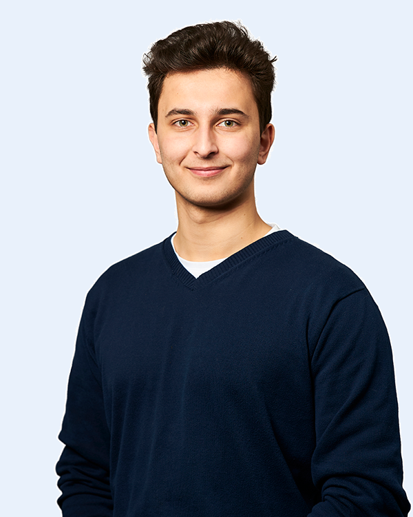 Smilende ung mand i mørkeblå sweater, frontportræt mod lys neutral baggrund