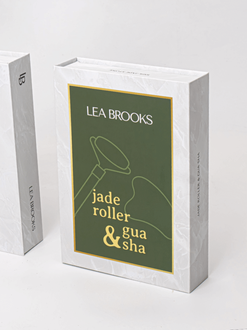 Lea Brooks jade roller og gua sha emballage, hvid marmorkasse med grøn etiket og gul tekst