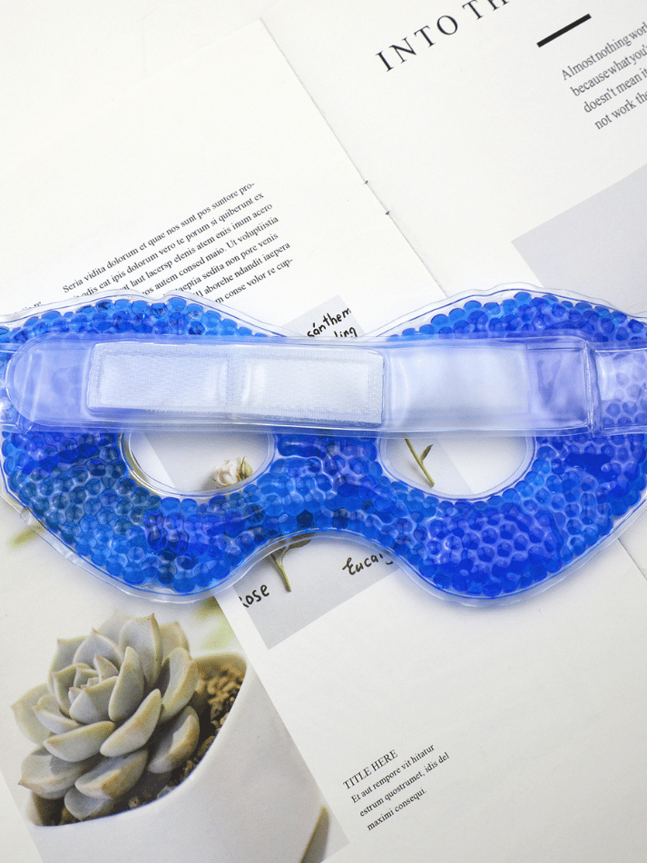 Blå gel øjenmaske med køleperler og justerbart velcrobånd lagt på åben magasinside
